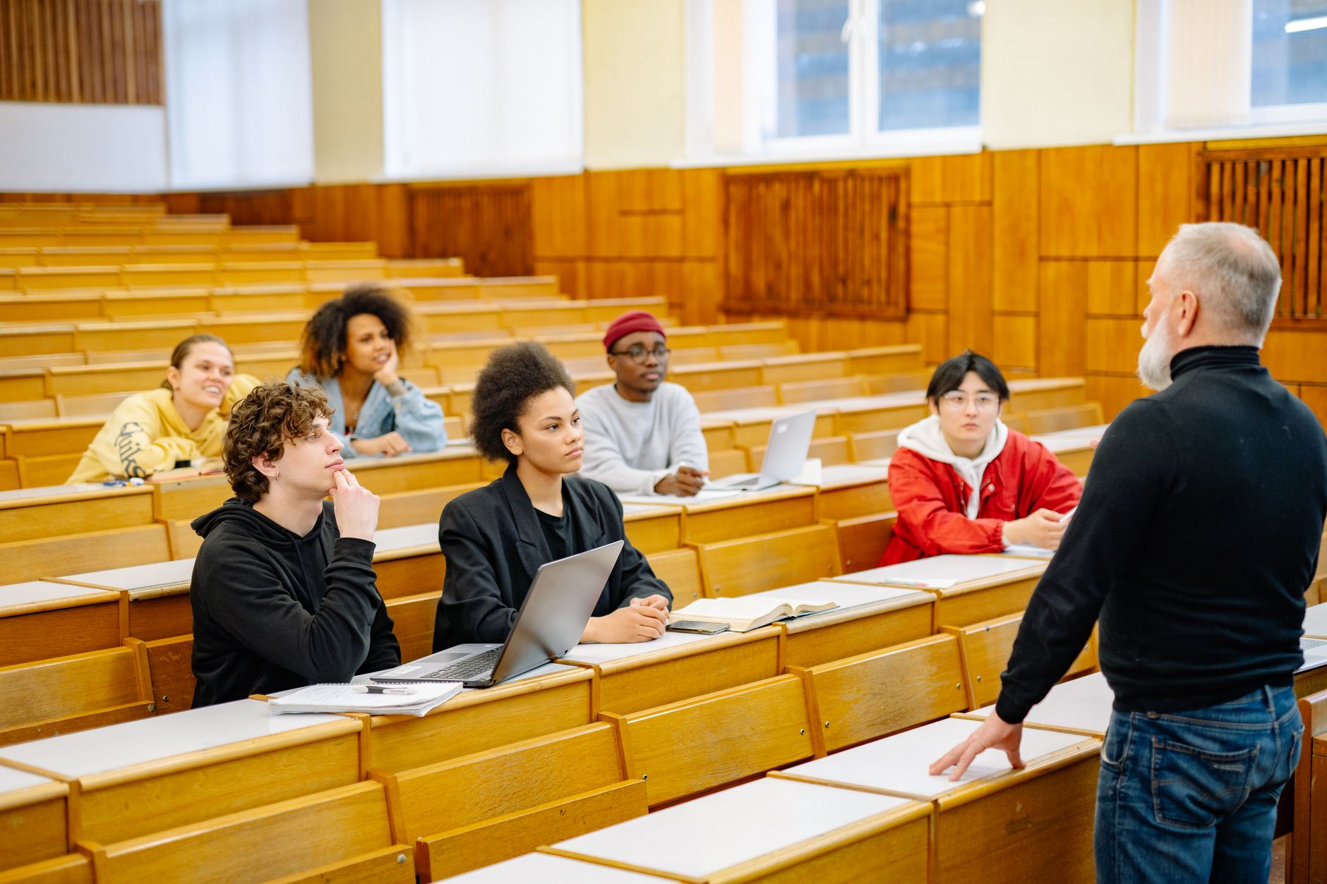 Graduate students with laptops listen to an instructor in a university lecture hall