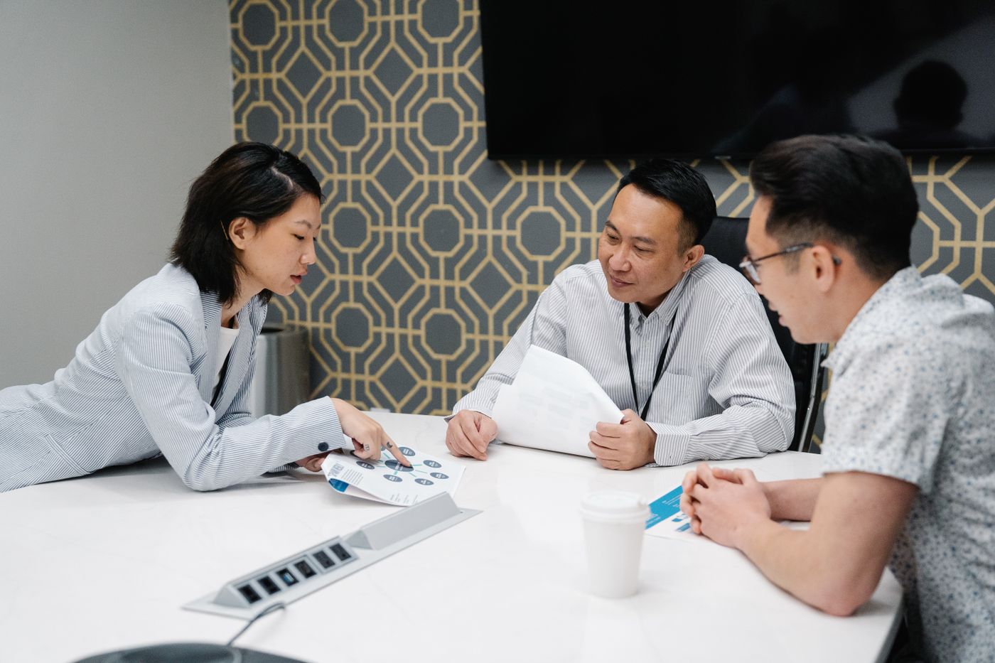 Three colleagues at a conference table review a printed diagram and notes