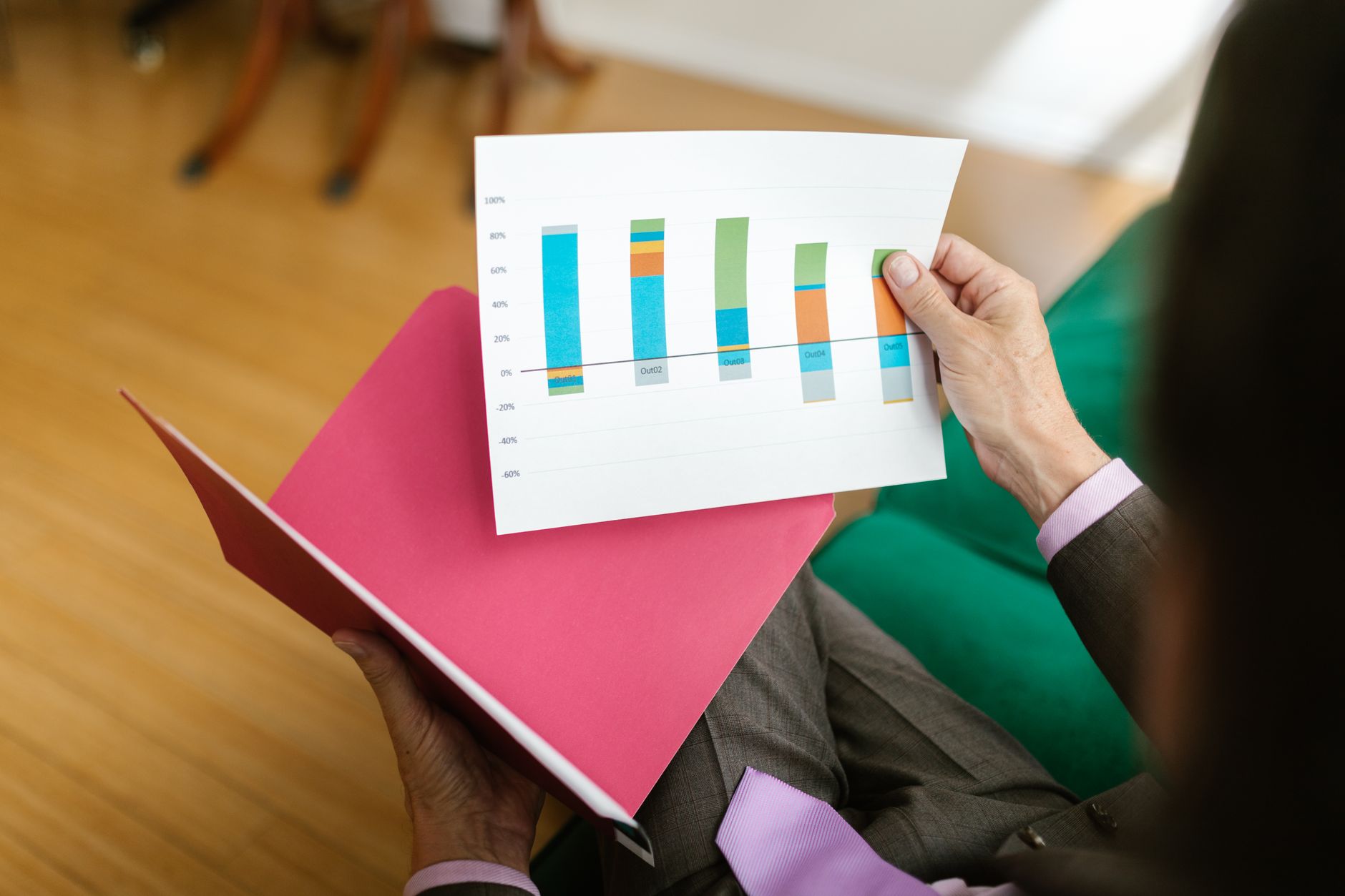 A manager in a suit holds a printed bar chart over an open pink folder while reviewing results