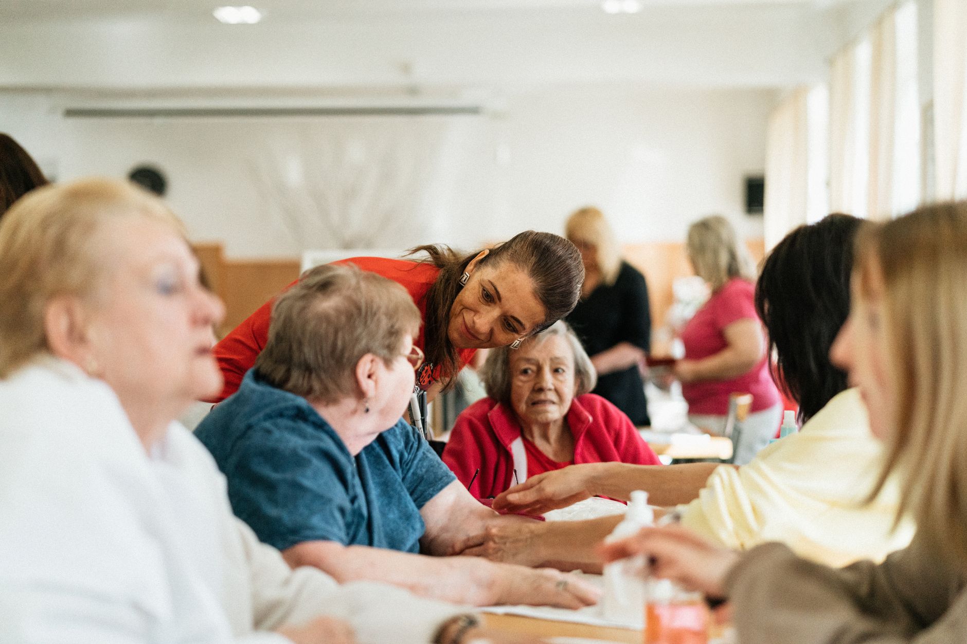 A staff member leans in to talk with older residents seated around an activity table in a care home